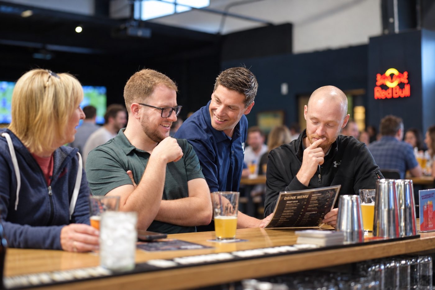 An owner leaning in over the drink menu with three guests seated at the bar