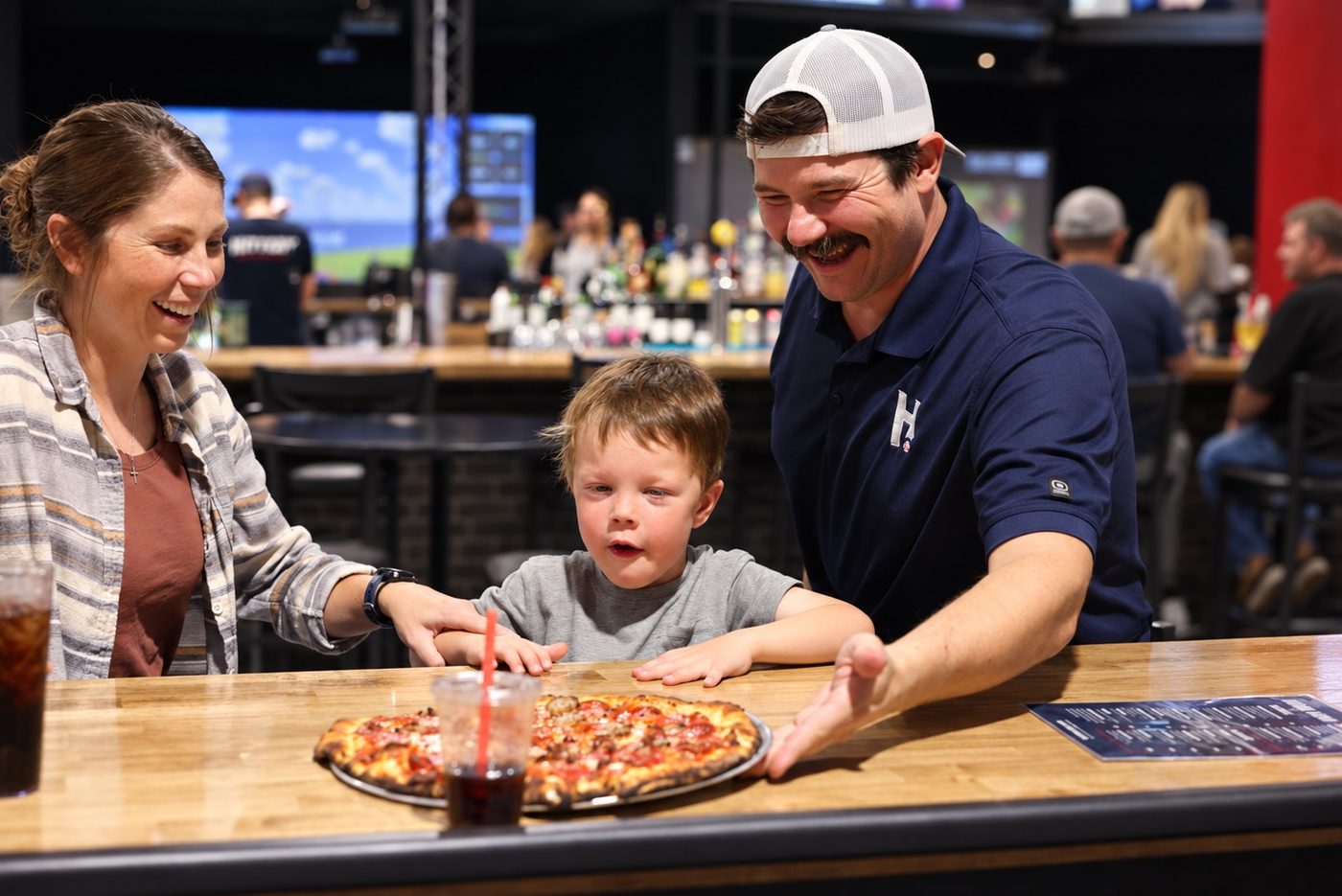 An owner presenting a pizza to a mother and her young son at the bar