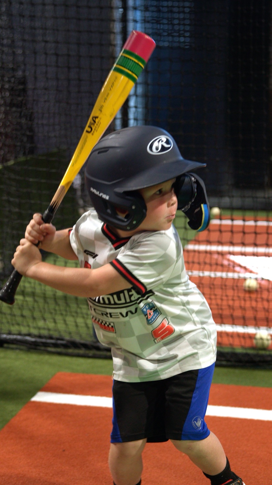 A young player mid-swing in the batting cage, locked in on the ball